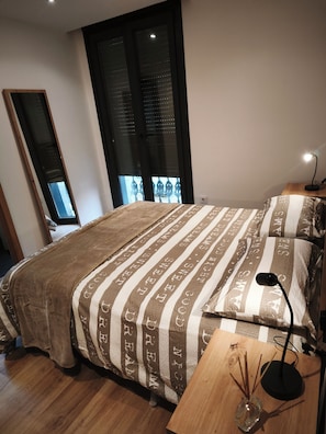 Ein Schlafzimmer mit einem Bett, einem Nachttisch, einer Lampe und einem Fenster mit Jalousien.