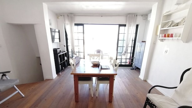 Een ruime kamer met een houten eettafel, witte stoelen, een zwarte bank en een boekenkast.
