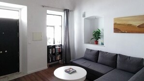 Een woonkamer met een bank, een rond bijzettafeltje, een boekenkast, een deur en een groot geweven plafond.