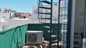 Een terras op het dak met een wenteltrap, een groene veiligheidshek en een airconditioning.