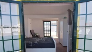 Een slaapkamer met een bed, een stoel, een kledingkast en een deur die naar een andere kamer leidt.