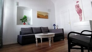 Een woonkamer met een rond geweven plafond, een grijze bank, een witte salontafel, een zwarte fauteuil en een schilderij aan de muur.