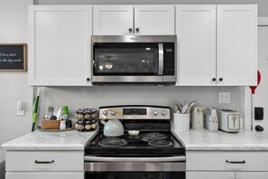 A kitchen with white cabinets, a stainless steel microwave, a stove, and various kitchen appliances. - The Magnolia Collective- Pet Friendly , 2 Kings , Exercise Equipment (Lynchburg)