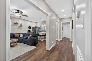 A modern living room with a sectional sofa, a ceiling fan, and a kitchen area in the background. - The Magnolia Collective- Pet Friendly , 2 Kings , Exercise Equipment (Lynchburg)