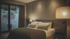Un dormitorio con cama, lámpara, vista al exterior con vegetación y pared con textura.
