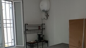 Une petite pièce propre, avec une table, un banc, un placard et une fenêtre grillagée.