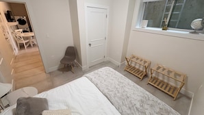 A bedroom with a bed, a chair, a door, a window, and a laundry area. - Peaceful Private Suite in Beautiful Home. 20 min to downtown (Burnaby)