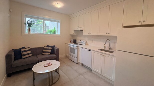 A compact kitchen with white cabinets, a dining area with a round table, and a window with a view of greenery. - Peaceful Private Suite in Beautiful Home. 20 min to downtown (Burnaby)
