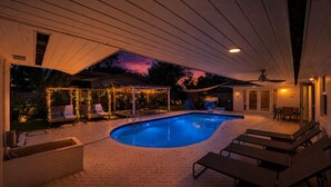 A swimming pool with lounge chairs, a covered patio, and string lights. - Villa Velvet ~ Heated Pool, Jacuzzi, Game Room & Minutes to Beaches (Pembroke Pines)