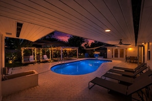 A swimming pool with lounge chairs, a covered patio, and string lights. - Villa Velvet ~ Heated Pool, Jacuzzi, Game Room & Minutes to Beaches (Pembroke Pines)
