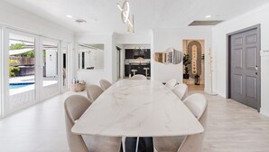 A modern kitchen with a central island, white cabinetry, and a view of the outdoor pool area. - Villa Velvet ~ Heated Pool, Jacuzzi, Game Room & Minutes to Beaches (Pembroke Pines)