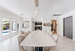 A modern kitchen with a central island, white cabinetry, and a view of the outdoor pool area. - Villa Velvet ~ Heated Pool, Jacuzzi, Game Room & Minutes to Beaches (Pembroke Pines)