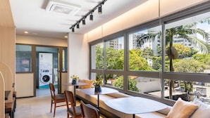 A modern hotel room with a large window, a sofa, and a table with chairs. - Studio Novo Campo Belo Piscina Congonhas Moema (São Paulo)