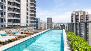 A rooftop swimming pool with lounge chairs, surrounded by high-rise buildings. - Studio Novo Campo Belo Piscina Congonhas Moema (São Paulo)
