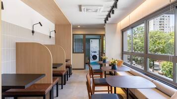 A modern hotel lobby with a seating area, a washing machine, and large windows offering a view of the city.