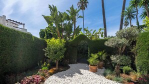 Un jardin avec un chemin de gravier, différentes plantes et une structure de bâtiment blanche.