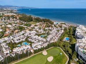 An aerial view of a coastal residential area with white buildings, a beach, and a golf course. - Golf & Beach Villa beside Guadalmina Golf Club — sleeps 8, lagoon style pool (Marbella)