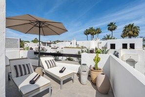 A rooftop terrace with white walls, a beige umbrella, two lounge chairs with striped pillows, and potted plants. - Golf & Beach Villa beside Guadalmina Golf Club — sleeps 8, lagoon style pool (Marbella)
