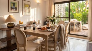 Un coin repas avec une table dressée pour six personnes, une lampe, des œuvres d’art encadrées et une vue sur la verdure par une grande fenêtre.