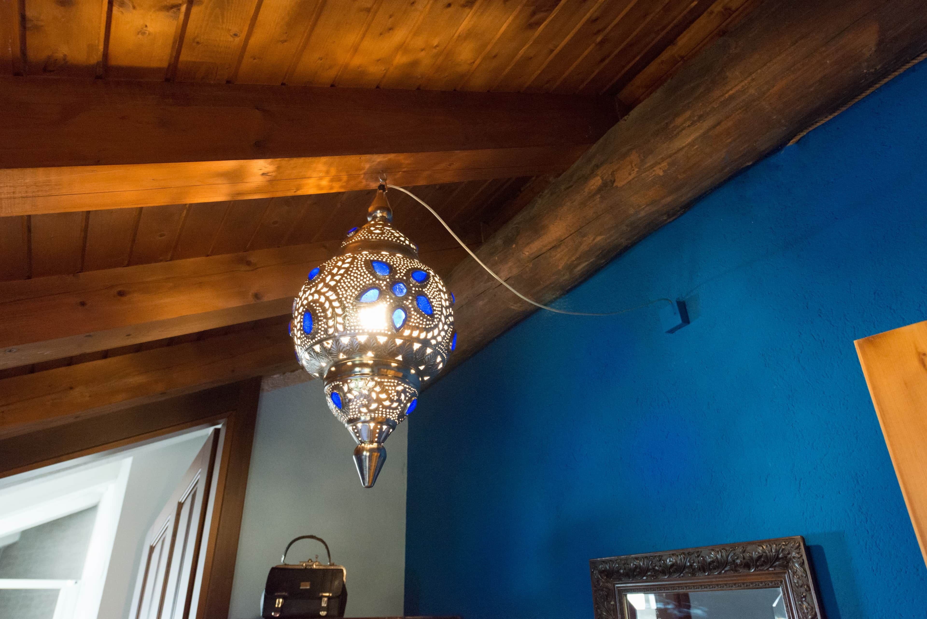 Un luminaire suspendu au design géométrique, un plafond en bois et un mur bleu.