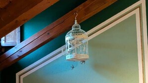 Une pièce avec un plafond en pente, deux fauteuils à motifs, une cage à oiseaux blanche suspendue et un mur vert avec des bordures blanches.