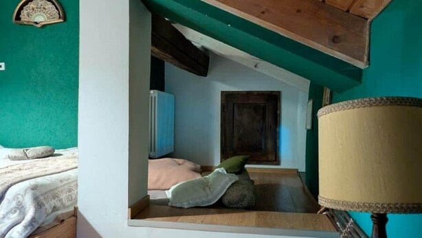 Une pièce avec un plafond en pente, des poutres en bois, un lit avec des oreillers, une table avec une lampe et un radiateur fixé au mur.