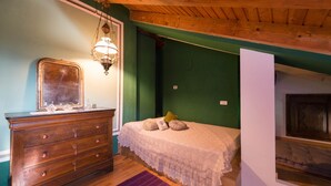 Une chambre avec une commode en bois, un lit recouvert d’une courtepointe blanche, un luminaire suspendu et un mur vert.