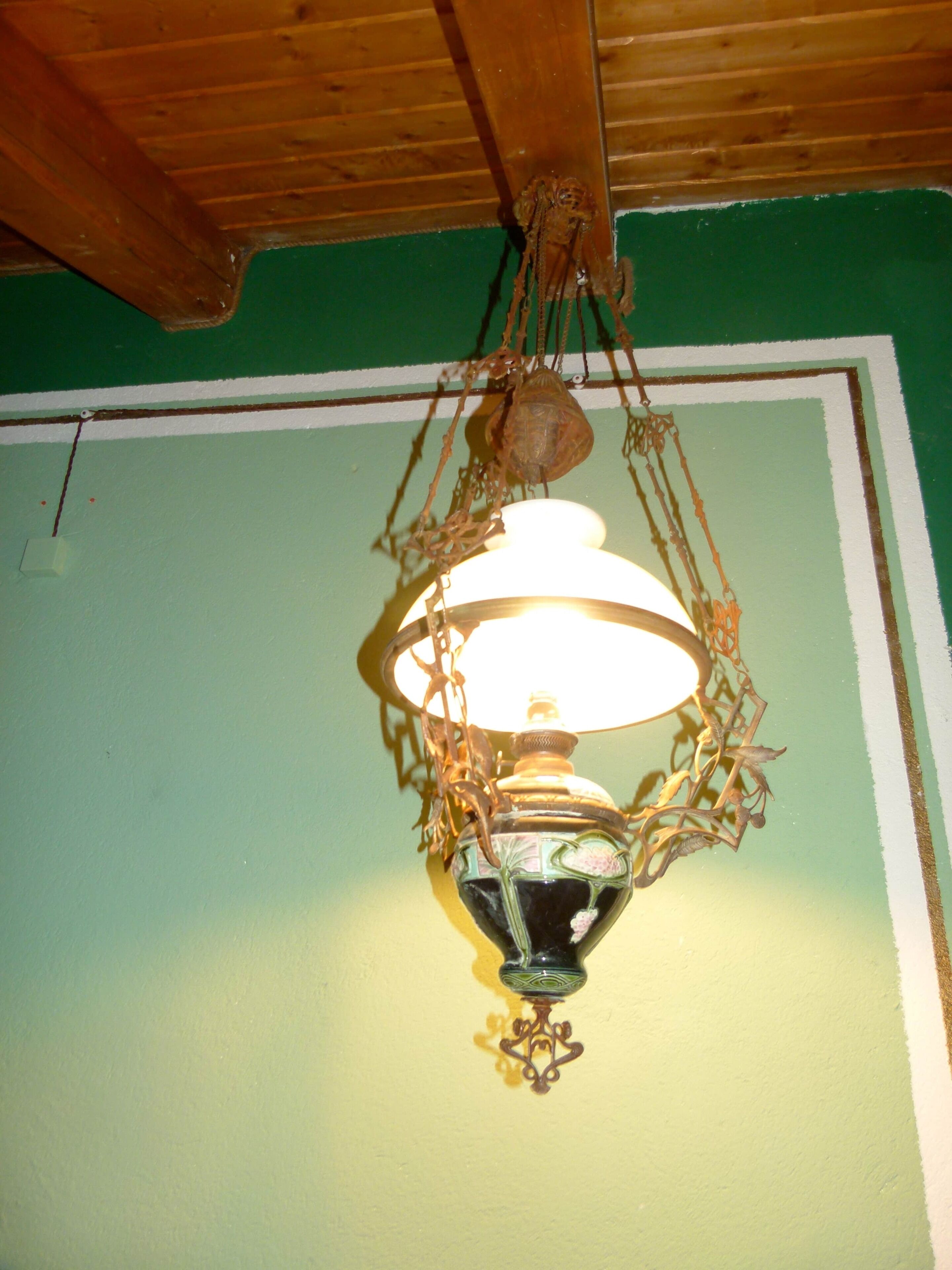 Een hanglamp met een glazen kap en een gloeilamp, bevestigd aan een groene muur met een houten plafond.