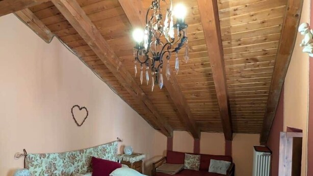A cozy attic bedroom with a wooden ceiling, a chandelier, a bed with floral bedding, and a small table with a decorative item. - Bizet Suite: Passion and Charm in "Red" (Villair-Amerique)