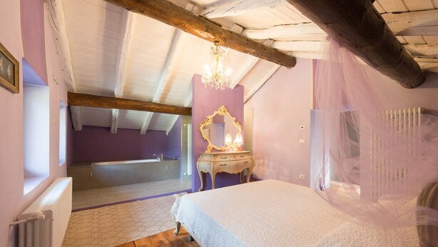 Een slaapkamer met een houten plafond, een wit bed, een kaptafel met spiegel en uitzicht op een badkamer.