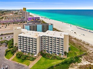 Ein mehrstöckiges Hotel mit Blick auf den Strand, einem Parkplatz und einem Poolbereich.