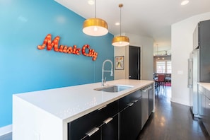 A modern kitchen with a blue accent wall, a white countertop, and a sink. - City Heights- Rooftop Patio, Skyline Views, Sleeps 10 Near Broadway (Nashville)