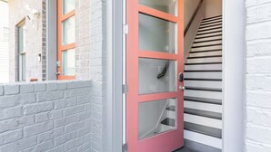 Une porte en verre à cadre rouge avec une poignée en métal, un mur en briques blanches et un escalier avec des marches noires.