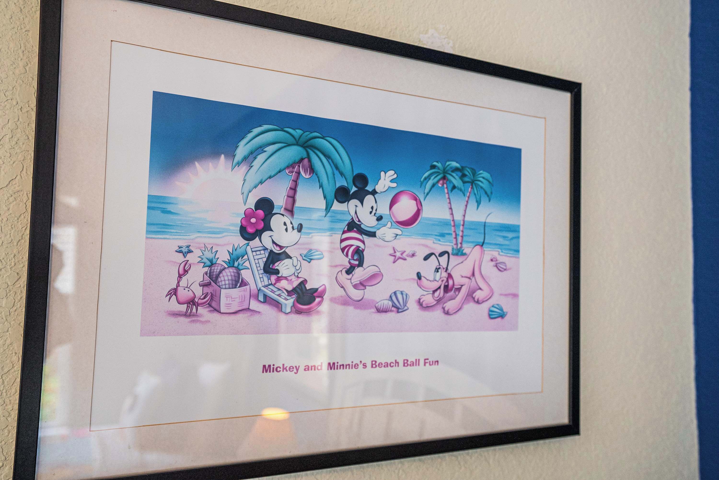 A framed picture of Mickey and Minnie at the beach with palm trees and the ocean in the background.