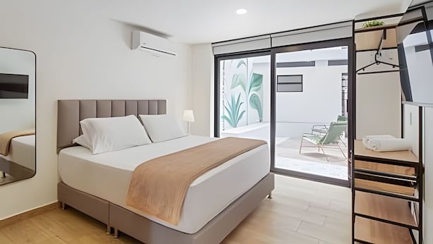 A modern hotel room with a bed, a desk, a chair, a wardrobe, and a balcony with a view. - Casa Velasquez 101 (Medellín)