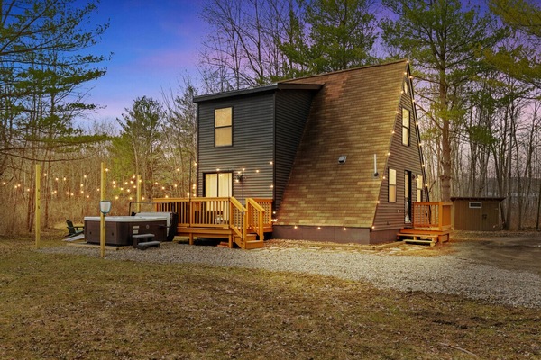 As evening sets in this A-frame cabin glows under string lights with a private hot tub and multiple deck areas ready for relaxing. Surrounded by trees and quiet it is the perfect spot to unwind and enjoy the outdoors