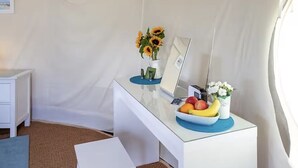 A white desk with a laptop, a vase of sunflowers, a bowl of fruit, and a small potted plant.