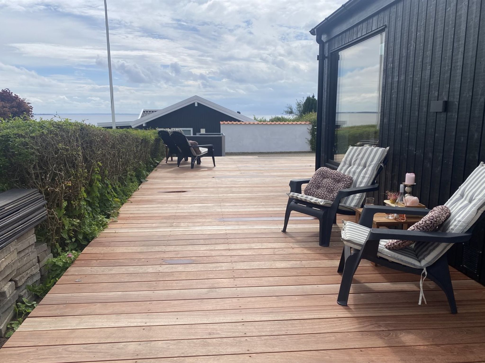 Um deck de madeira com área de estar externa, vista para o mar e um edifício moderno com grandes janelas.