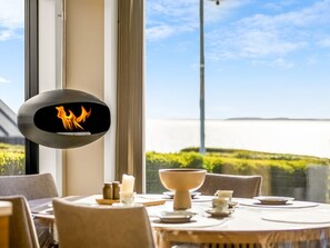 Ein Essbereich mit Tisch für vier Personen, einem Kamin und Blick auf das Meer.