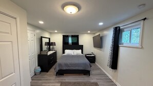 Un dormitorio con cama, cómoda, espejo, televisor y ventana.