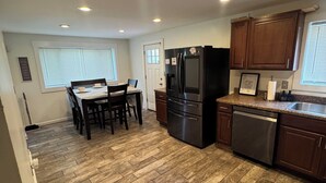 Una cocina equipada con refrigerador, lavavajillas, armarios de madera y un comedor con sillas y una mesa.