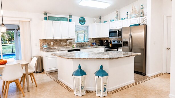 A modern kitchen with white cabinets, a central island, a stainless steel refrigerator, and decorative items. - Stylish Seahorse Villa in Cape Coral with Heated Pool (Cape Coral)