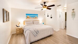 A bedroom with a bed, nightstand, ceiling fan, wall art, and a door leading to another room. - Stylish Seahorse Villa in Cape Coral with Heated Pool (Cape Coral)