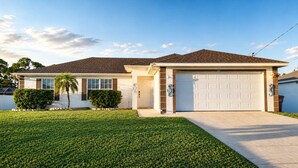 A two-story house with a garage, a well-maintained lawn, and a clear sky. - Stylish Seahorse Villa in Cape Coral with Heated Pool (Cape Coral)