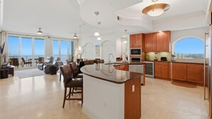 A spacious living area with a large island, a dining area with chairs, and a kitchen with wooden cabinets and a large window. - Mustique 2001 (Gulf Shores)