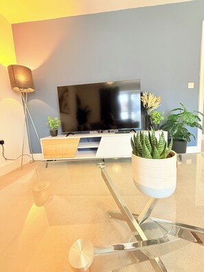 Una sala de estar moderna con un televisor de pantalla plana, una mesa de centro de vidrio y varias plantas en macetas.