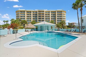 Um hotel com uma piscina grande, palmeiras e uma estrutura com telhado de palha.