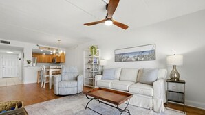 A living room with a sofa, a coffee table, a ceiling fan, a lamp, and a painting. - Ocean Breeze West 705 (Pensacola)