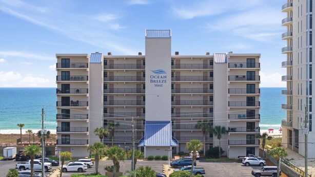 A multi-story hotel with balconies, a parking lot, and a view of the ocean. - Ocean Breeze West 705 (Pensacola)