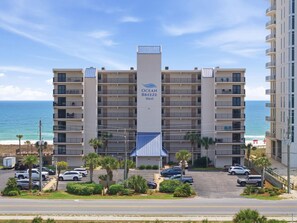 A multi-story hotel with balconies, a parking lot, and a view of the ocean. - Ocean Breeze West 705 (Pensacola)